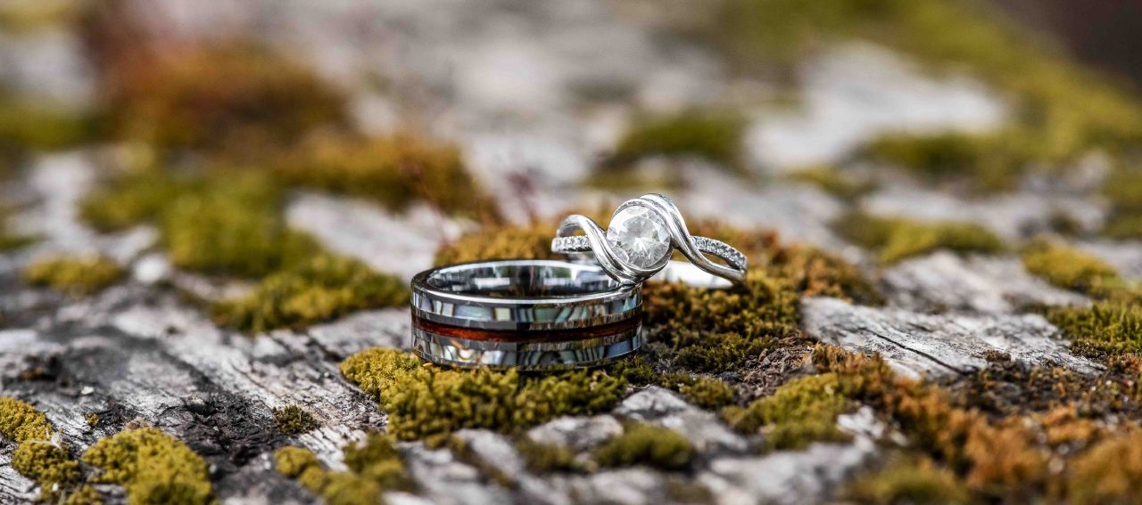 A photo of two unique looking wedding rings, on a mossy log.