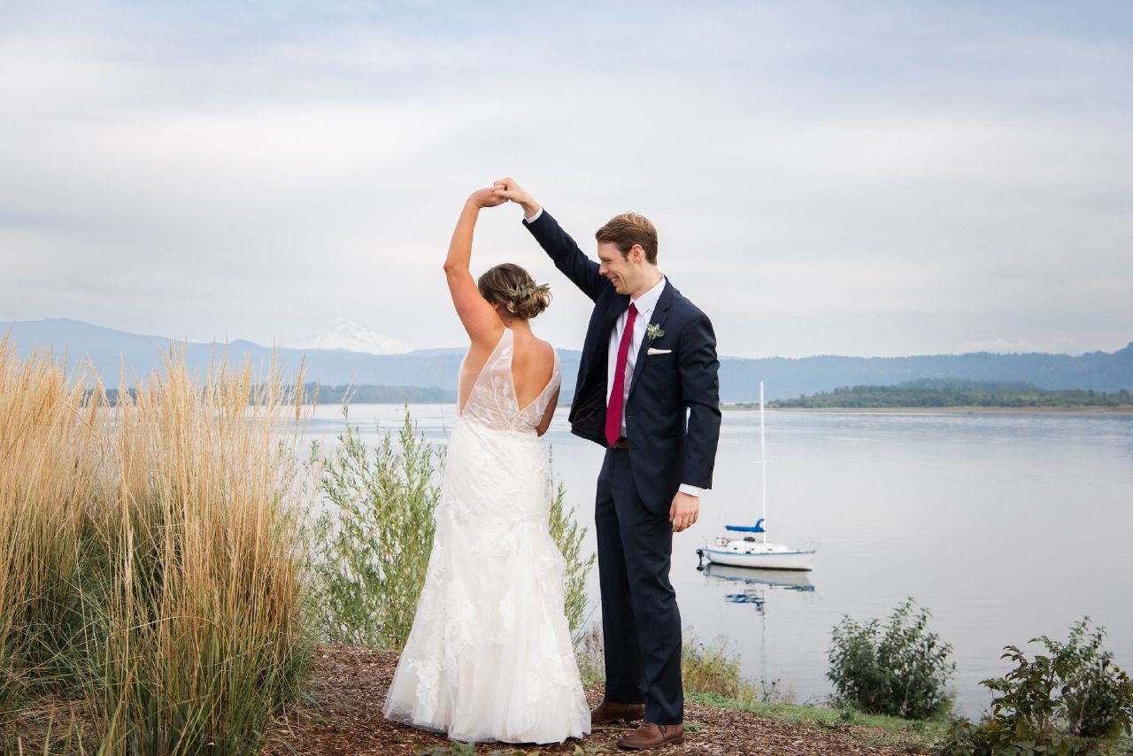 A bride and groom outside, dancing with Mt hood and the columbia river and sailboat in the background