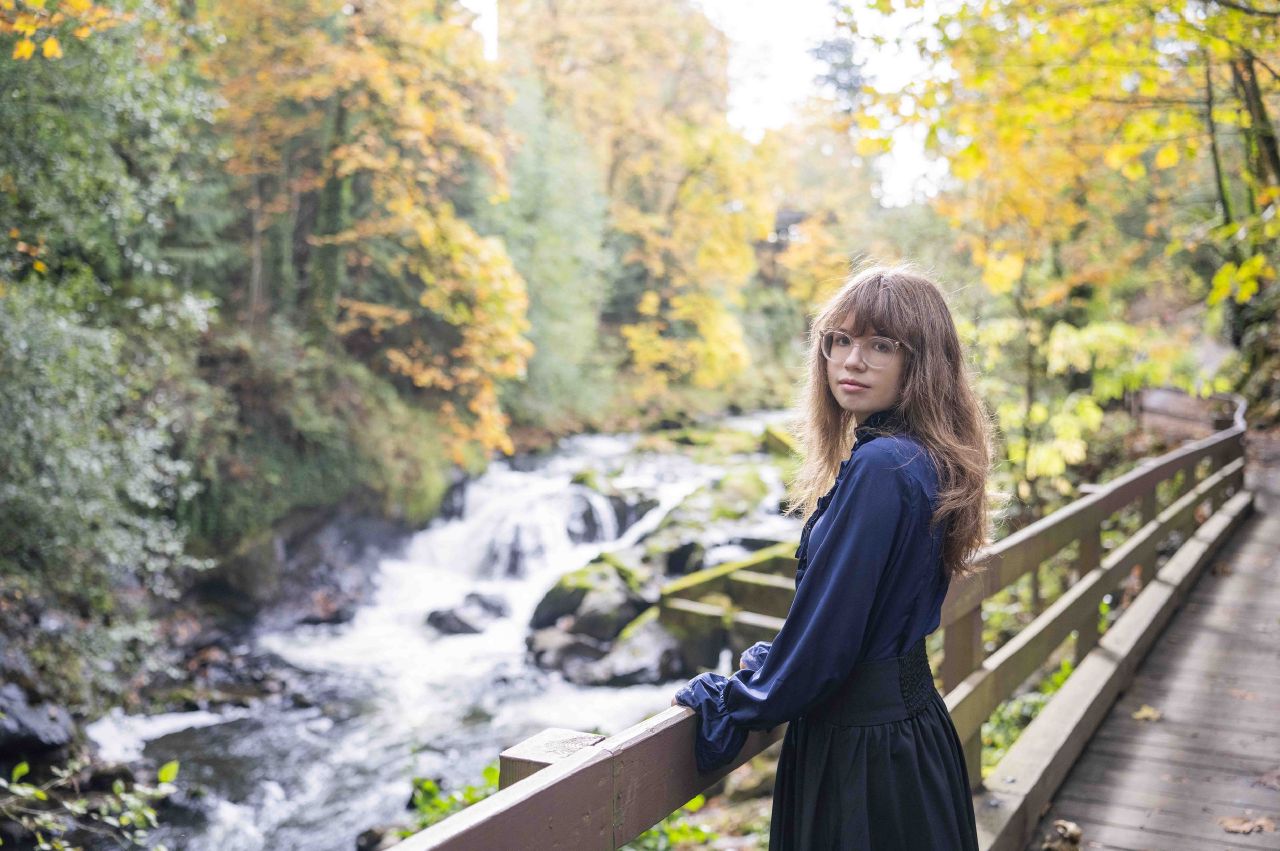 A woman in a vintage blue blouse and black maxi skirt holding a handrail on a bridge
