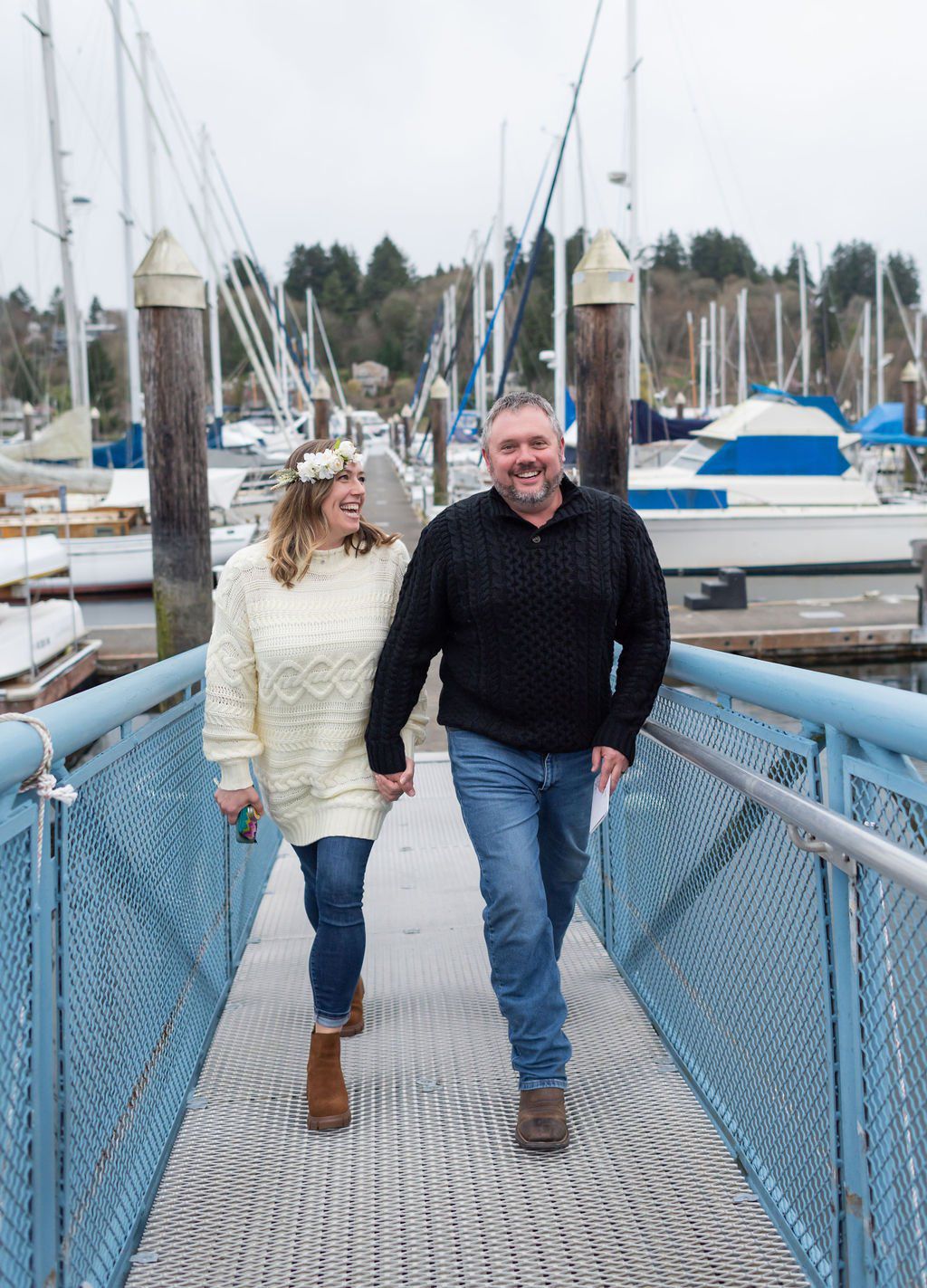 A wedding couple walking up a dock ramp at a marina with sailboats in the background