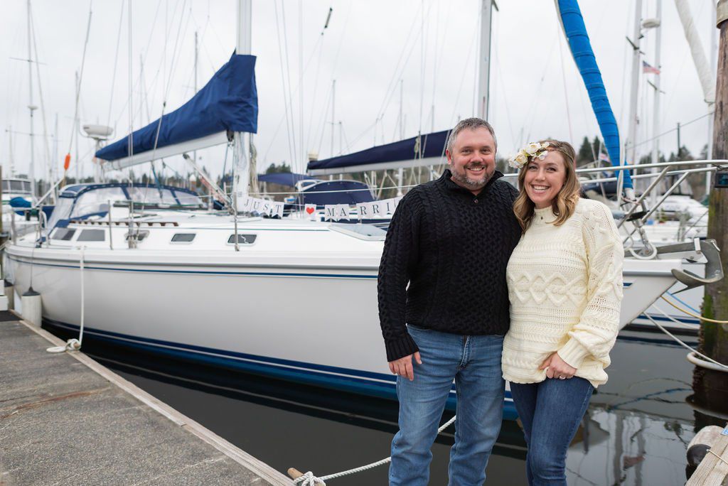A wedding couple smiles in front of a sailboat that says Just Married
