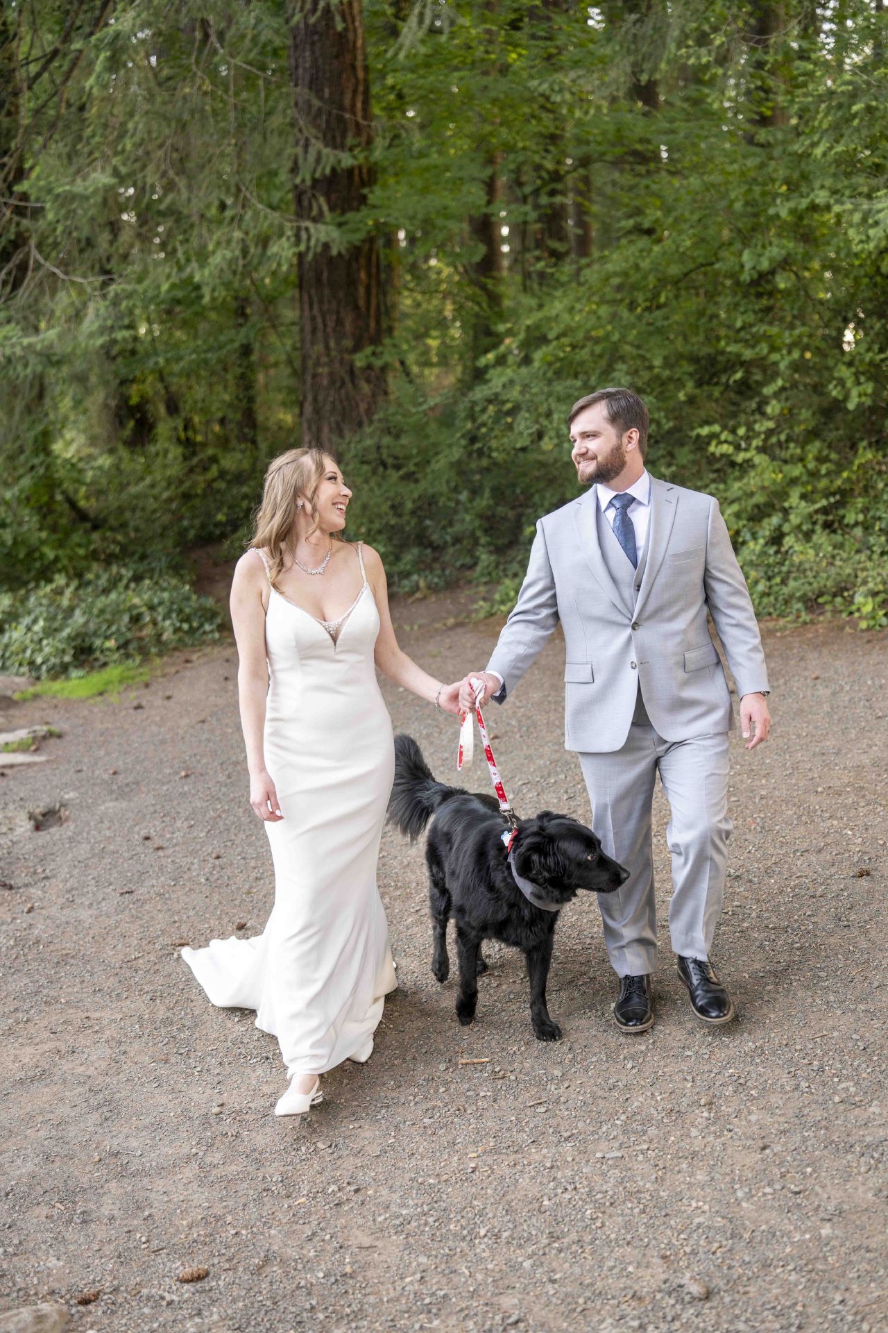 Bride and groom walk their black dog through wooded trails at Lacamas Lake Park Camas Washington wedding.