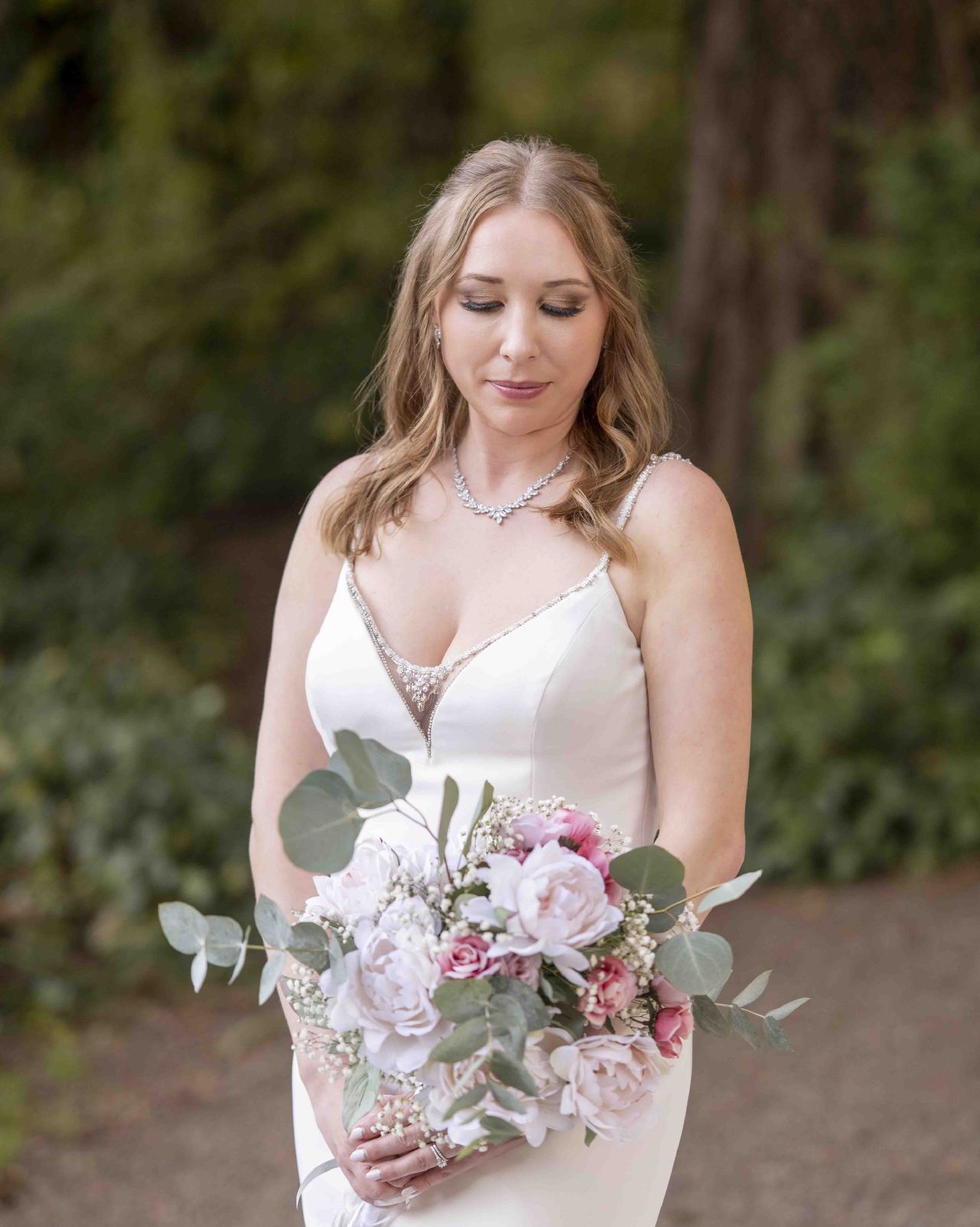 Bride smiling in forest path at Lacamas Lake Park, holding blush bouquet during Camas WA wedding portraits.